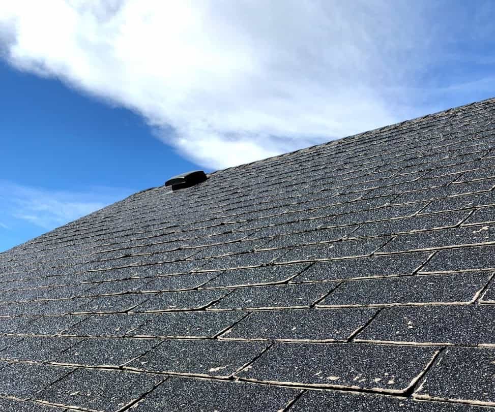 Picture of a roof with worn out shingles needing repair with the sky in the background