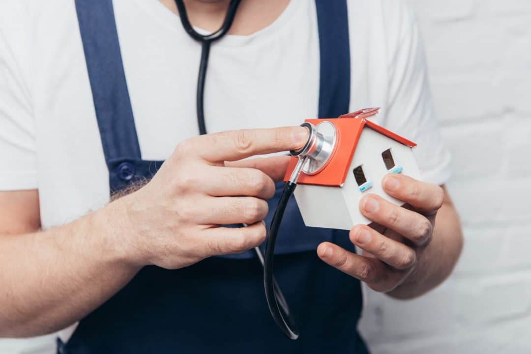 a man in overalls using a stethoscope checking the top of a roof illustrating roof inspections.