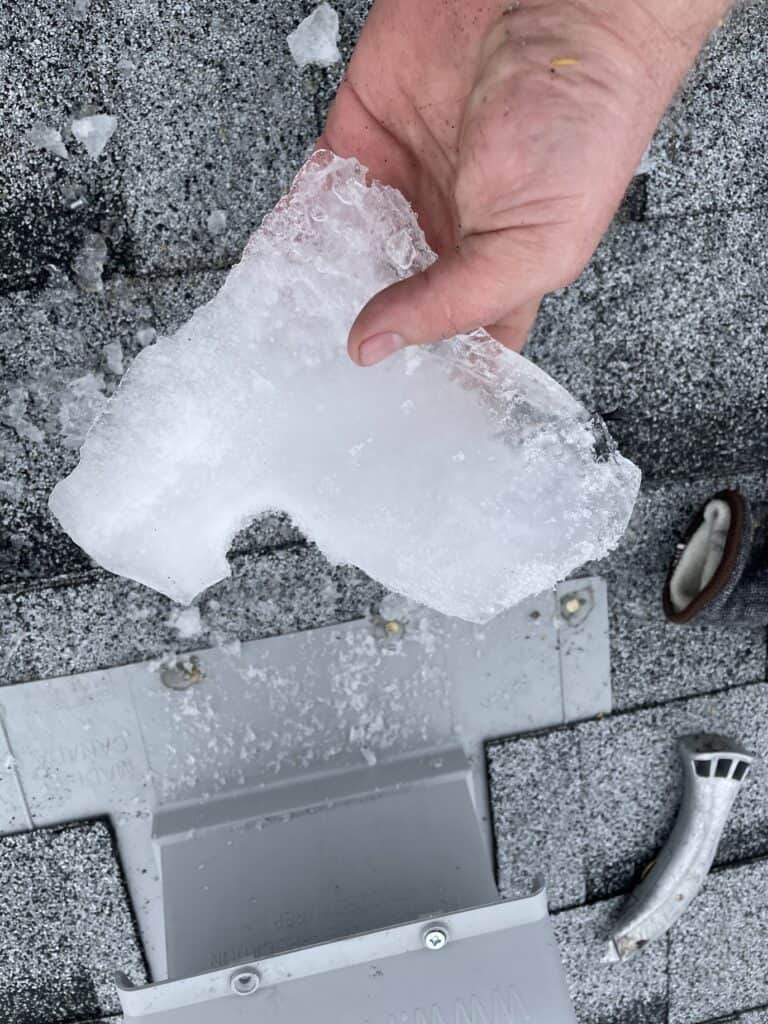 A roofer holding a piece of ice from a vent