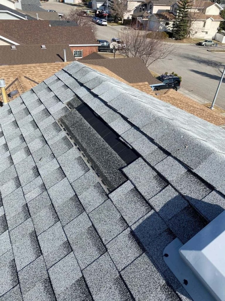 More missing shingles, possibly from storm damage on a roof in Calgary from the perception of a roofer on top of the roof.